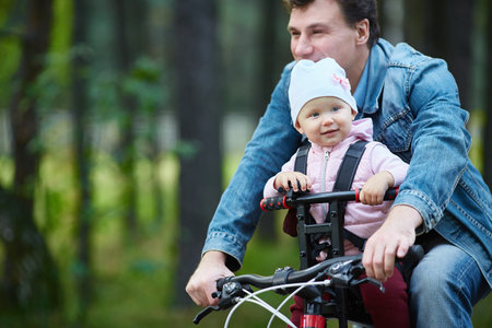 The child is sitting in the bicycle seat of the parentの写真素材