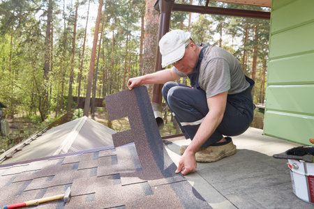 A man lays a roof of soft tiles on the roof of a country house.の写真素材