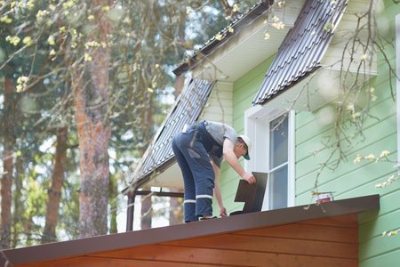 View from the window of the cottage. A person working on the roof installs a soft roof.