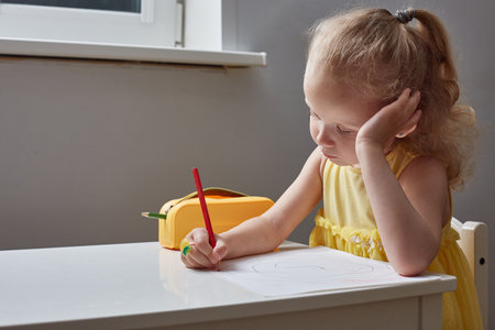 A bored girl draws with pencils at table at home.の写真素材