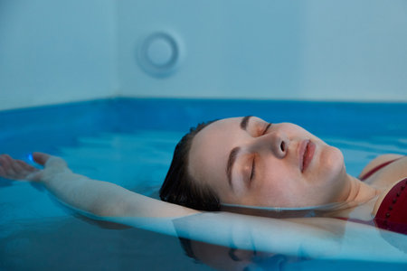 Beautiful woman floating in tank filled with dense salt water used in meditation, therapy, and alternative medicine.の写真素材