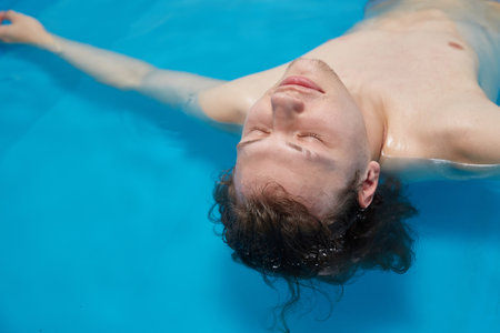 Handsome young man is swimming in the pool on his back. Relaxation and spa therapy. Copy Spaceの写真素材