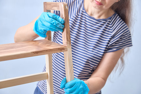 A woman paints a wooden shelf with oil. DIY repairs. Renovated wooden furniture.