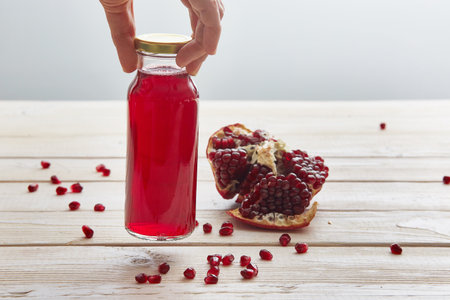 hand picks up a small glass bottle of pomegranate juice from a wooden tableの写真素材