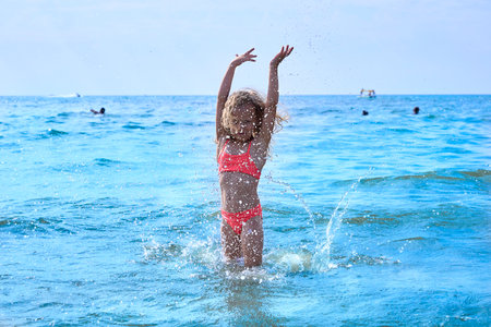 Summer vacation, a happy smiling little girl splashing in the seaの写真素材
