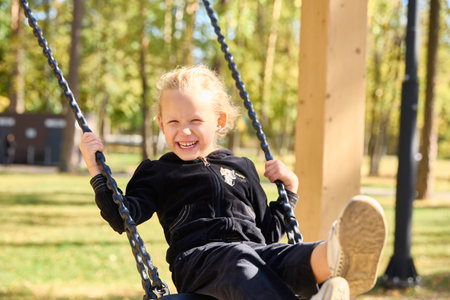 A laughing little girl is swinging on a swing on a sunny autumn dayの写真素材