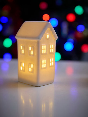 Ceramic house decoration with glowing windows captured with vibrant bokeh effect. Festive atmosphere highlighting warmth and holiday cheer. Perfect for seasonal themes.の写真素材