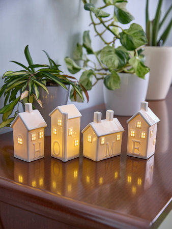 Ceramic house-shaped lanterns spell HOME as they emit a warm glow on a table, surrounded by potted green plants, creating a cozy and inviting atmosphere in the home.の写真素材