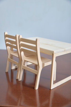 Two miniature wooden chairs are placed beside a small wooden table on a desk. The setup highlights the craftsmanship and design of tiny furniture models, suitable for decor or educational purposes.の写真素材