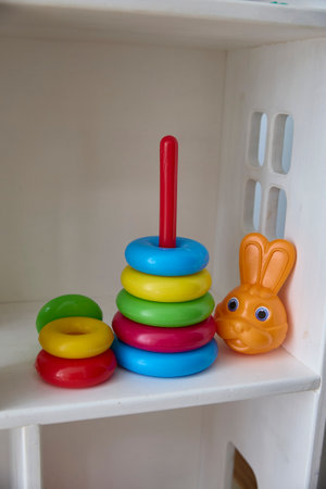 Colorful stacking rings on a red pole sit alongside an orange plastic toy rabbit, displayed on a white shelf. Ideal for showcasing children's toys or educational play items.の写真素材