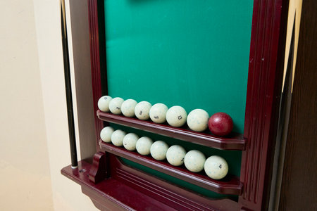 Billiard scoreboard showcasing a collection of numbered white balls and a single red ball on a green felt background, neatly arranged on wooden shelves.の写真素材