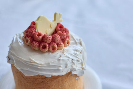 Capturing springtime joy, a beautifully adorned kulchy boasts creamy frosting and ripe raspberry garnish, illuminated by winter light.の写真素材