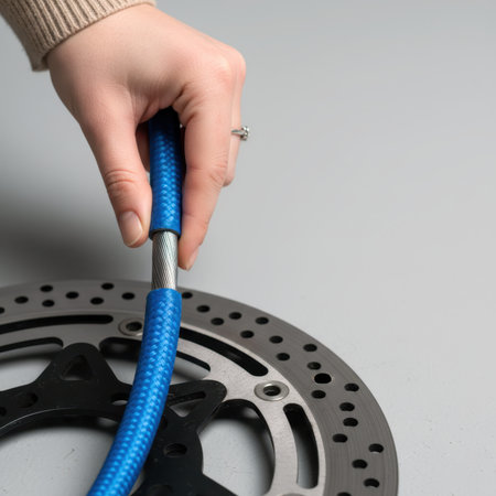 Hand holding a braided steel brake line above a motorcycle disc brake rotor.の素材