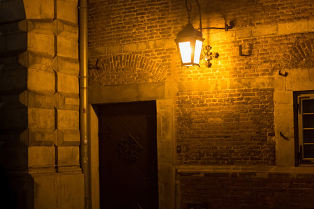 The old medieval brick wall of historical building with illuminated night lamp.の写真素材