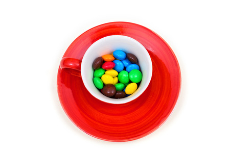 Red cup with colorful button-shaped chocolates on the white background.の写真素材