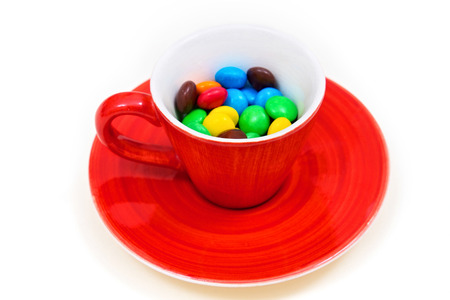 Red cup with colorful button-shaped chocolates on the white background. の写真素材