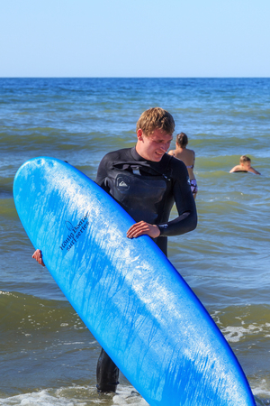 ZELENOGRADSK, KALININGRAD REGION, RUSSIA - JULY 29, 2017: Unknown surfer with surfboard standing in the blue water of Baltic Sea at summer time.のeditorial素材