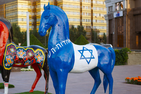 ASTANA, KAZAKHSTAN - JULY 25, 2017: Art installation with figure of horse painted in israel ethnic ornament in Astana on Nurzhol Boulevard with modern building on the background.のeditorial素材