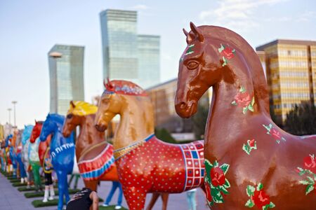 ASTANA, KAZAKHSTAN - JULY 25, 2017: Art installation with figures of horses painted in different ethnic ornament in Astana on Nurzhol Boulevard with modern high-rise buildings on the background.のeditorial素材