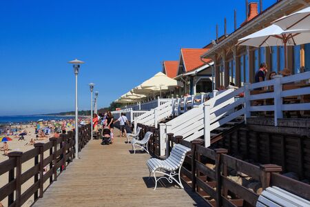 ZELENOGRADSK, KALININGRAD REGION, RUSSIA - JUNE 18, 2019: Unknown people resting on a sandy beach on the Baltic Sea coast in famous resort Zelenogradsk (formerly known as Cranz) near wooden restaurantのeditorial素材