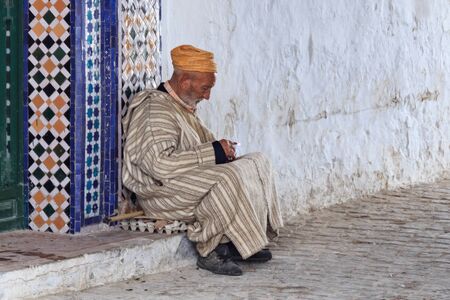TETOUAN, MOROCCO - MAY 24, 2017: Unknown old man in national moroccan clothes resting near wall on the one of the streets of Tetouan Medina in Northern Morocco.のeditorial素材