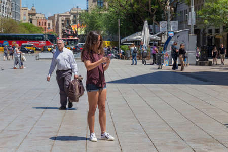 BARCELONA, SPAIN - MAY 15, 2017: Unknown young attractive woman with cellphone standing on the Placa Nova street (near Barcelona Cathedral) in historical center of Barcelona in sunny day.のeditorial素材