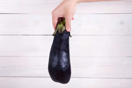 Purple eggplant in a human hand on white wooden background.の写真素材