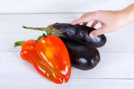 Purple eggplants and bulgarian peppers in a human hand on white wooden background.の写真素材