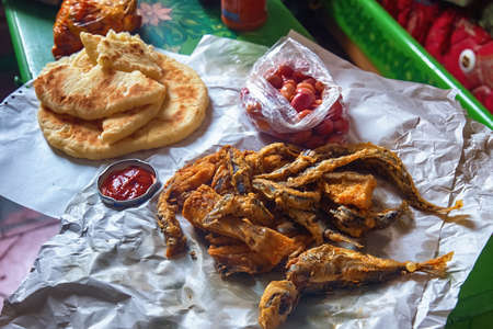 Deep fried sardine lies on oiled paper and near lies pickled olives, tomato sauce and flatbread.の写真素材