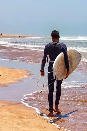 Unknown man in a wetsuit walking holding a surfboard in his hands along the Atlantic coast....