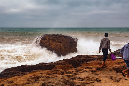 View of the unknown young people walking near stormy water of the Atlantic Ocean in the area of Essaouira in Morocco.の写真素材