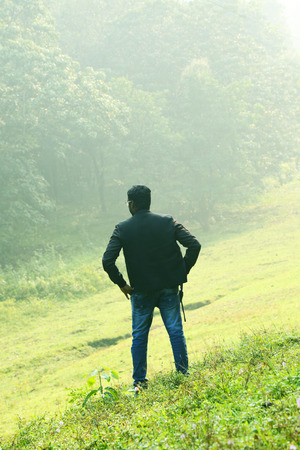 Happy businessman standing pose and turning back upon camera. With a beautiful green scenery of park on backgroundの写真素材