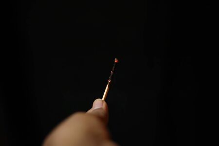 Burnt extinguished match held in hand on black rugged backgroundsの写真素材