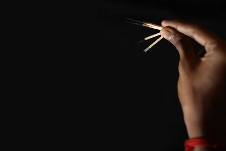 Hand holding an extinguished matchstick on black background.の写真素材