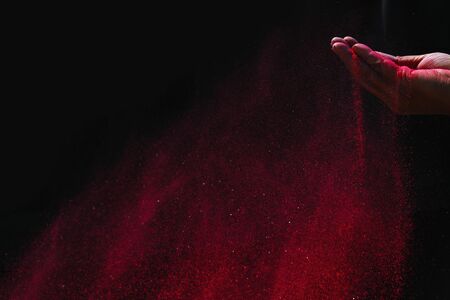 Closeup hand red colour holi powder splash at black backgroundの写真素材