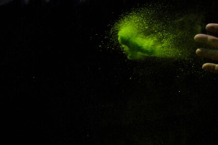 Closeup hand green colour holi powder splash at black backgroundの写真素材