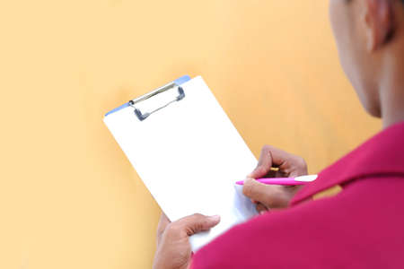 Photo pour Close up of a young mechanic writing on a clipboard on a white and gray backgrounds - image libre de droit