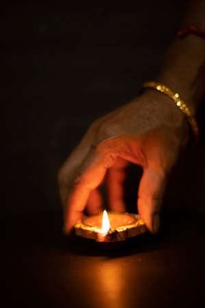 Happy diwali - Hand holding or lighting or arranging diwali diya or clay lamp in dark background,