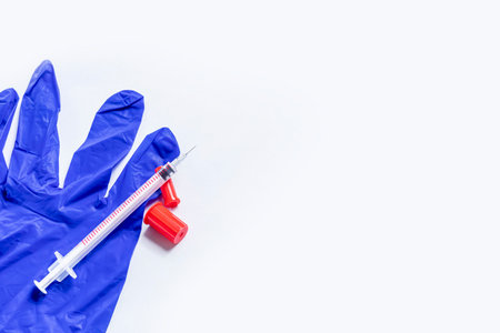 Disposable syringe and rubber gloves on white background, top view
