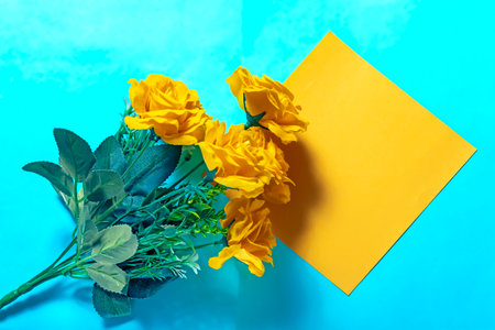 Bouquet of yellow roses and a yellow sheet of paper on a blue backgroundの写真素材