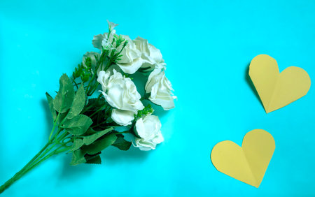 White roses and yellow paper hearts on blue background. Valentine's day concept.
