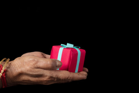 Close up shot of Indian female hands holding a small gift box on a black background.の写真素材