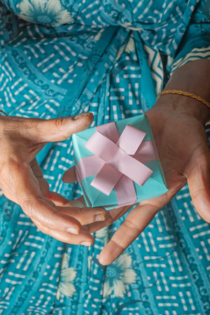 Beautiful Indian woman in saree holding blue gift box in hand with pink bow, closeupの写真素材
