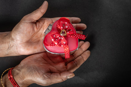 Female hands holding a heart shaped gift box with a red ribbon on a black background. Top view, close-upの写真素材