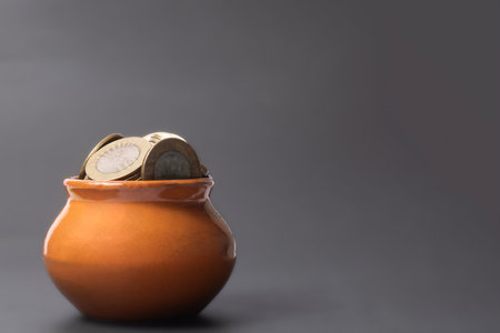 Coins in a clay pot on a gray background with copy space. Saving concept.の写真素材