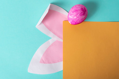 Easter greeting card with rabbit ears and yellow egg on blue background, space for textの写真素材