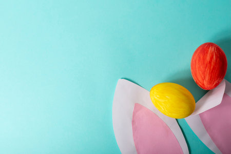 Colorful Easter eggs and pink rabbit ears on blue background, space for text, flat lay