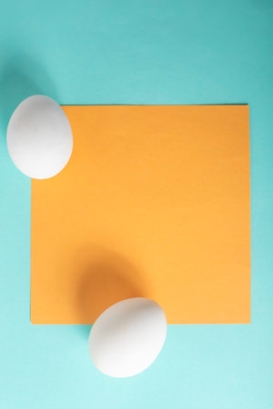 Two white eggs and a yellow sheet of paper on a blue background. Top viewの写真素材