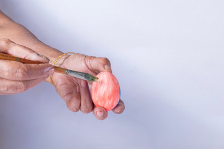 Hand of an indian woman holding an Easter egg and painting with a paintbrush on a white backgroundの写真素材