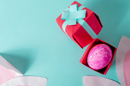 Top view of pink easter egg in gift box and rabbit ears on blue background